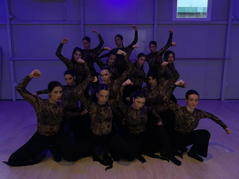 Un gruppo di ballerine in costume di pizzo, in posa sotto la luce viola