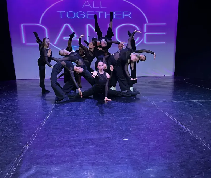 Un gruppo vestito di nero in una figura d’insieme, davanti all’insegna di All Together Dance