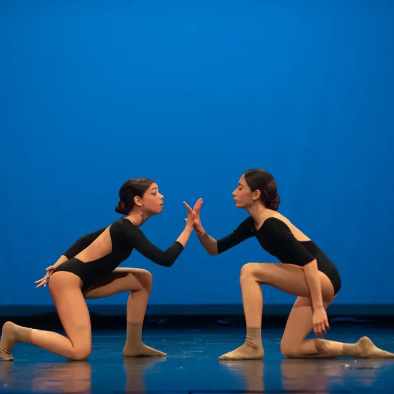 Due ballerine in body nero, inginocchiate una di fronte all’altra, palmo contro palmo