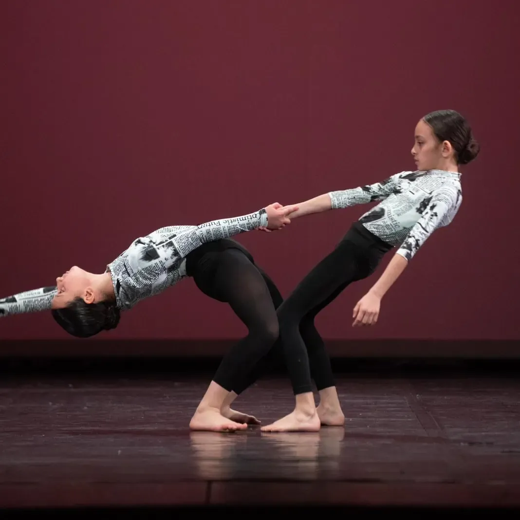 Un passo a due sul palco: due ballerine si tengono per mano, in equilibrio all’indietro