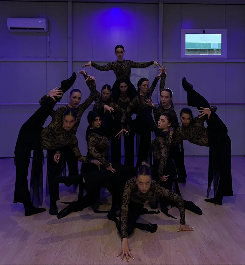 Un gruppo in costume di pizzo forma una piramide con le braccia, sotto la luce viola