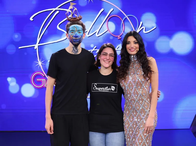 Un ragazzo con il viso dipinto, accanto alla sua truccatrice e alla conduttrice